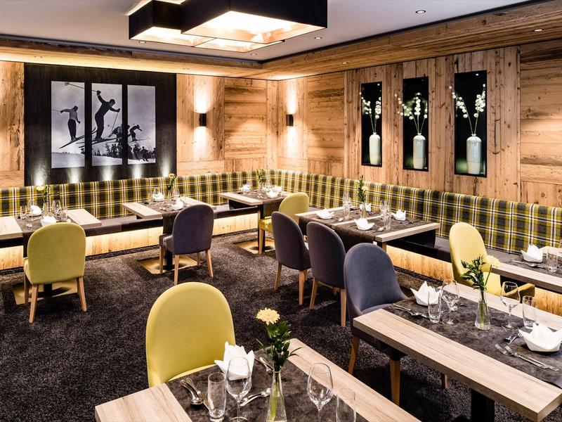 Pohodlná hotelová lounge s dřevěnými stěnami, kostkovanými lavicemi a barevnými židlemi.