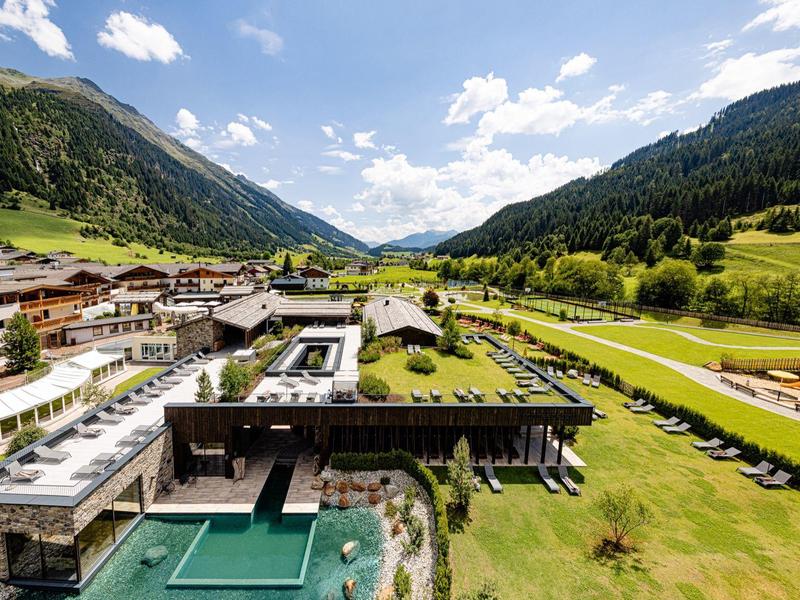 Moderní hotel s venkovním bazénem obklopený zelenými loukami a horami v údolí.