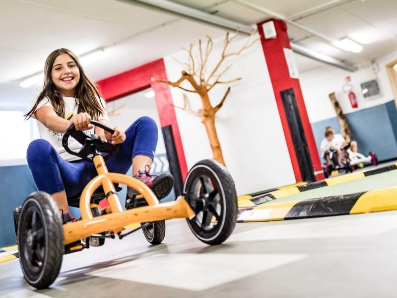 Mladá dívka jezdí na šlapacím vozítku v světlé, moderní vnitřní herně.