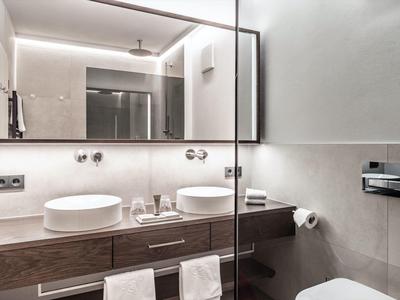 Moderne hotelbadkamer met dubbele wastafels, grote spiegel, glazen douche en houten wastafelmeubel.