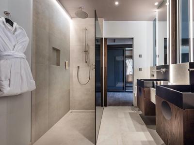 Moderne hotelbadkamer met inloopdouche, dubbele wastafels en badjassen aan de muur.