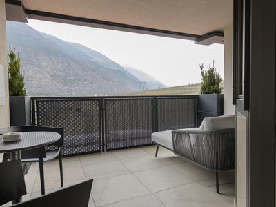Balkon met stoelen en tafel met uitzicht op bergen en deels bewolkte lucht.