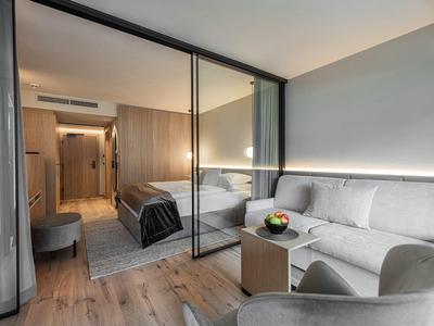 Moderne hotelkamer met houten vloer, glazen scheidingswand, bed, bank en fauteuil.