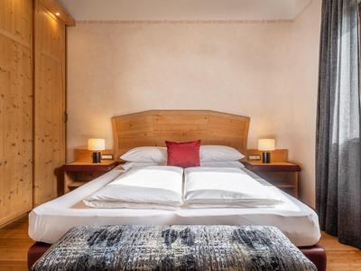 Hotelkamer met tweepersoonsbed, houten hoofdeinde, nachtkastjes, lampen en een rood kussen.