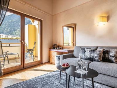 Knusse hotelkamer met grijze bank, salontafel en balkon met uitzicht op de bergen.