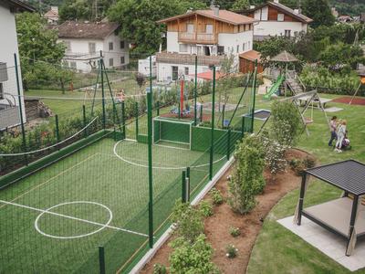 Kleine eingezäunte Sportanlage mit Fußballfeld im Garten eines Hotels in ländlicher Umgebung.