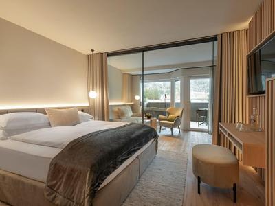 Moderne hotellkamer met groot bed, zithoek, glazen scheidingswand en warm licht.