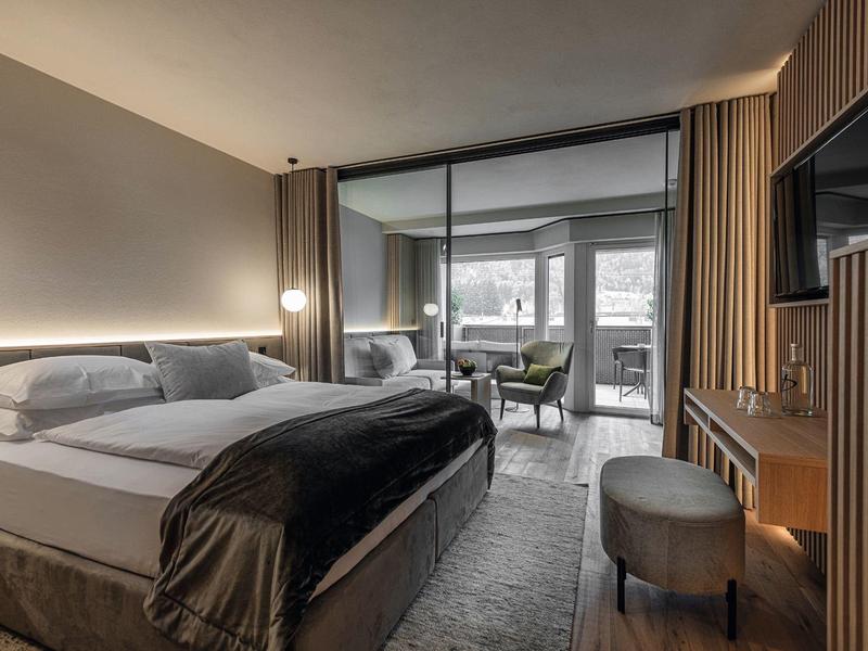 Moderne hotelkamer met groot bed, sfeerverlichting, tv en werkplek bij het raam.