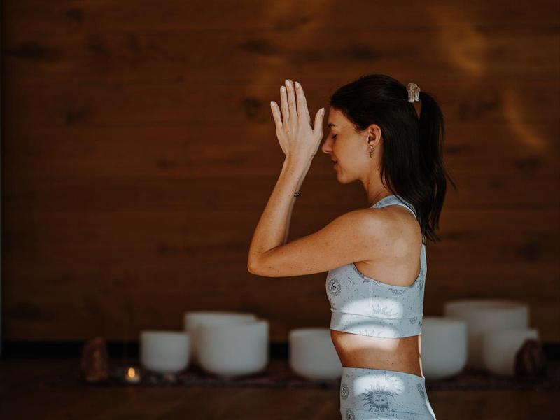 Vrouw in gestreepte outfit mediteert knielend in warme, houten kamer met zacht licht en kussens.