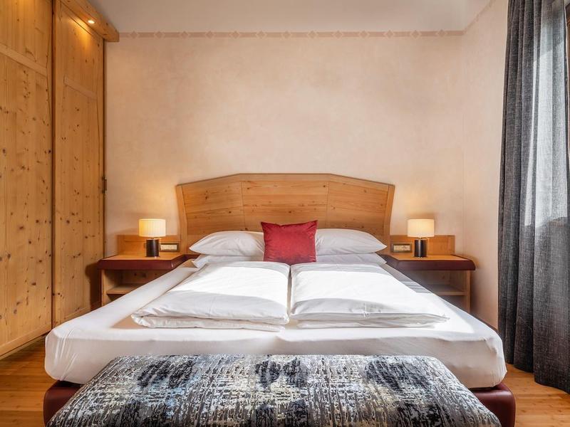 Hotelkamer met tweepersoonsbed, houten hoofdeinde, nachtkastjes, lampen en een rood kussen.