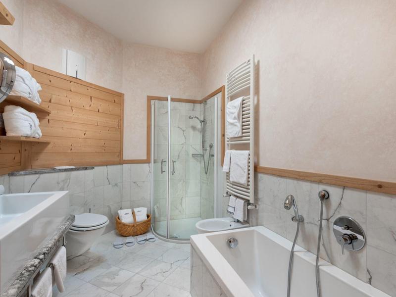 Moderne hotelbadkamer met glazen douche, wit bad, handdoekverwarmer en houten accenten.