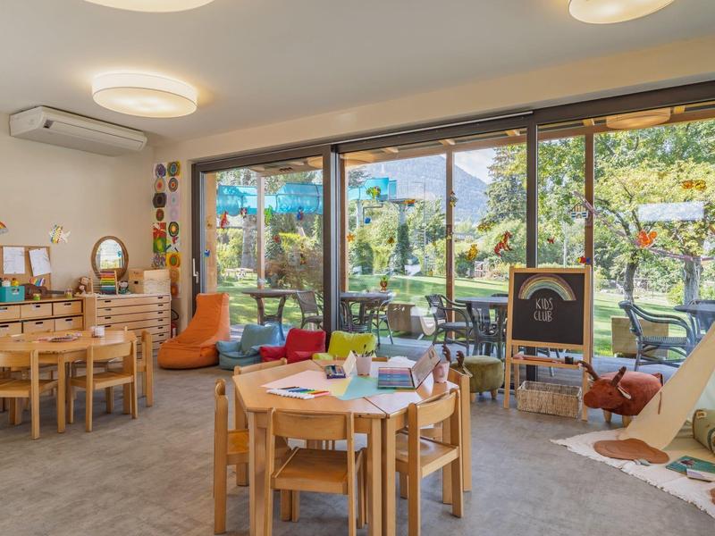 Lichte, gezellige speelkamer voor kinderen met houten meubels en grote ramen met uitzicht op een tuin.