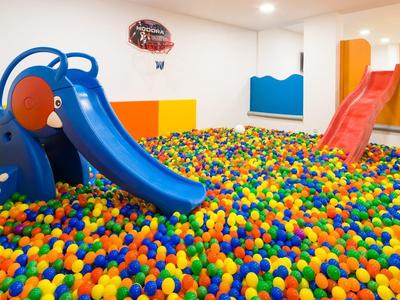 Heldere, kleurrijke ballenbak met twee kleine glijbanen in een binnenruimte.