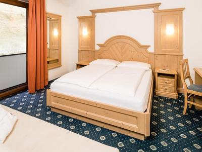 Lichte hotelkamer met tweepersoonsbed, bureau, stoel en warme houten meubels.