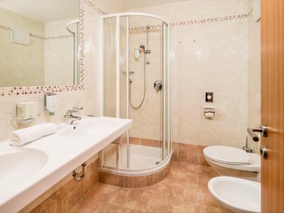 Lichte badkamer met wasbak, ronde glazen douchedeur en toilet in warme beige- en bruintinten.