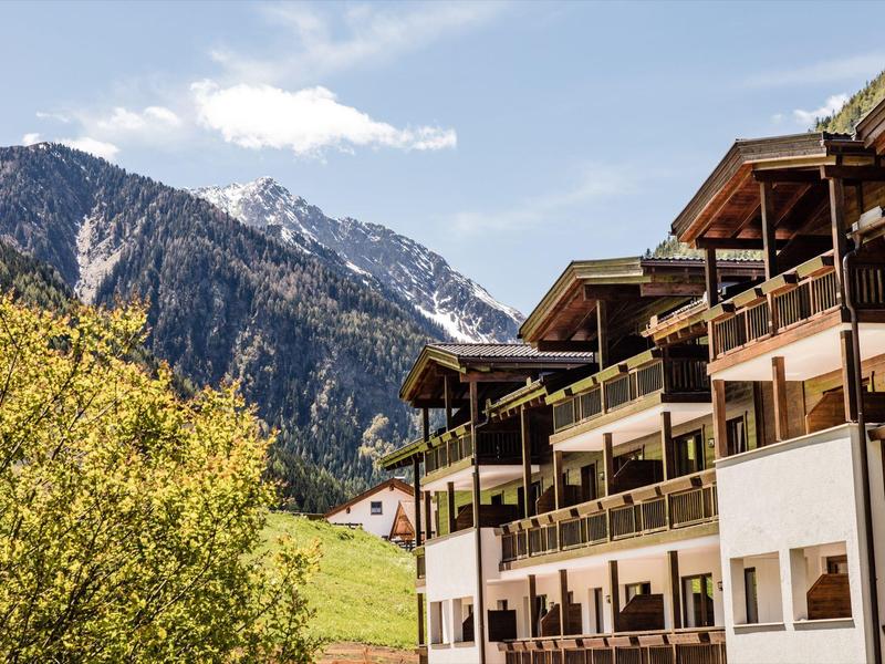 Bergresort met balkonkamers en besneeuwde toppen op de achtergrond onder een blauwe lucht.