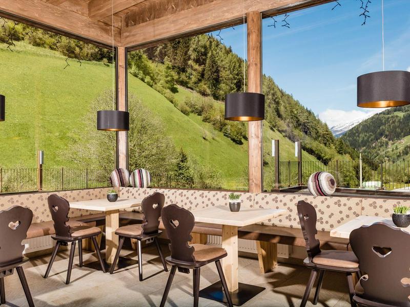 Gezellig restaurantgedeelte met houten meubels en panoramisch uitzicht op groene bergen.