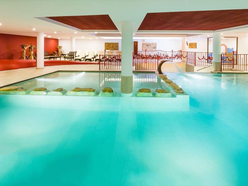 Modern binnenzwembad met jacuzzi en zithoek in de lichte wellnessruimte van een hotel.
