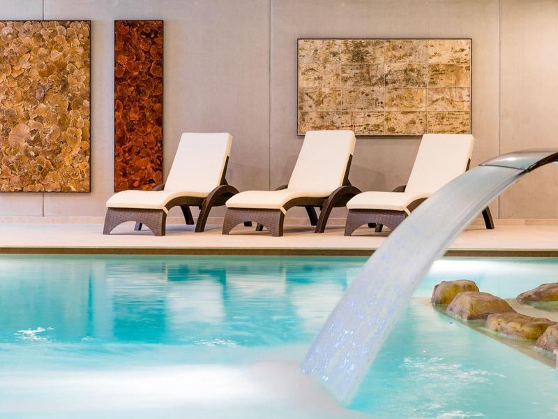 Moderne binnenzwembad met waterstraal en ligstoelen voor decoratieve wandkunst.