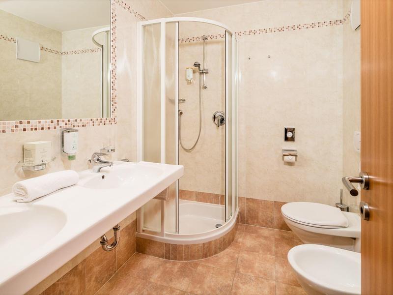 Lichte badkamer met wasbak, ronde glazen douchedeur en toilet in warme beige- en bruintinten.