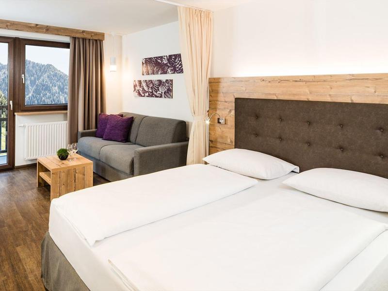 Lichte hotelkamer met tweepersoonsbed, houten vloer en balkon met uitzicht op de bergen.