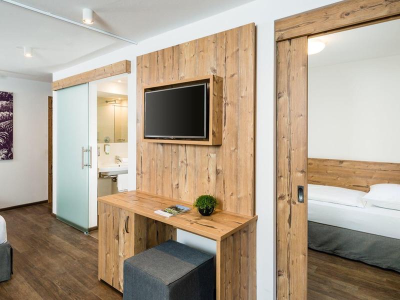 Moderne hotelkamer met houten accenten, wand-tv en spiegel aan de deur.