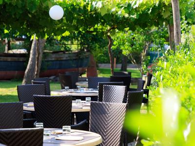 Außerbereich mit Tischen und Stühlen unter grünem Blätterdach, ideal für Restaurantgäste.