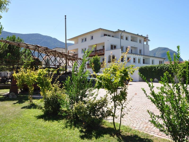 Hotelgebouw met tuin, planten en bergen op de achtergrond bij zonnig weer.