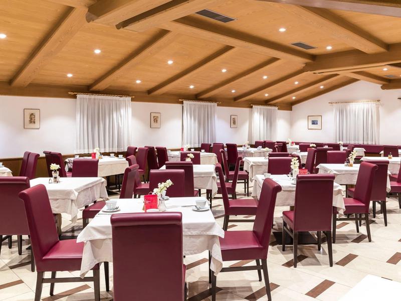 Grote eetzaal met gedekte tafels en rode beklede stoelen in een hotel.