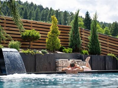 Ein entspannter Mann liegt an einem modernen Pool mit Wasserfällen und begrünten Hecken.