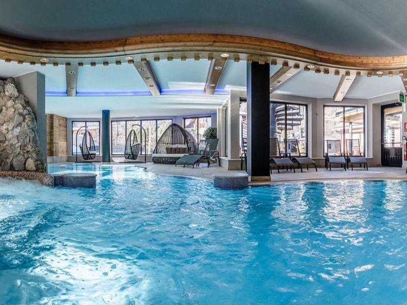 Grande piscina coperta con soffitto curvo, parete in pietra e aree relax.