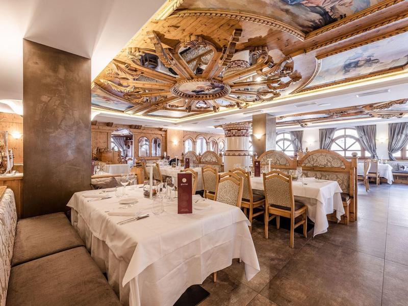 Ristorante elegante con tavoli apparecchiati, sedie di legno e soffitto dipinto artisticamente.