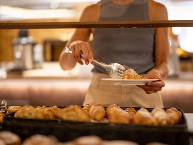 Persona con grembiule si serve al buffet della colazione con prodotti da forno.