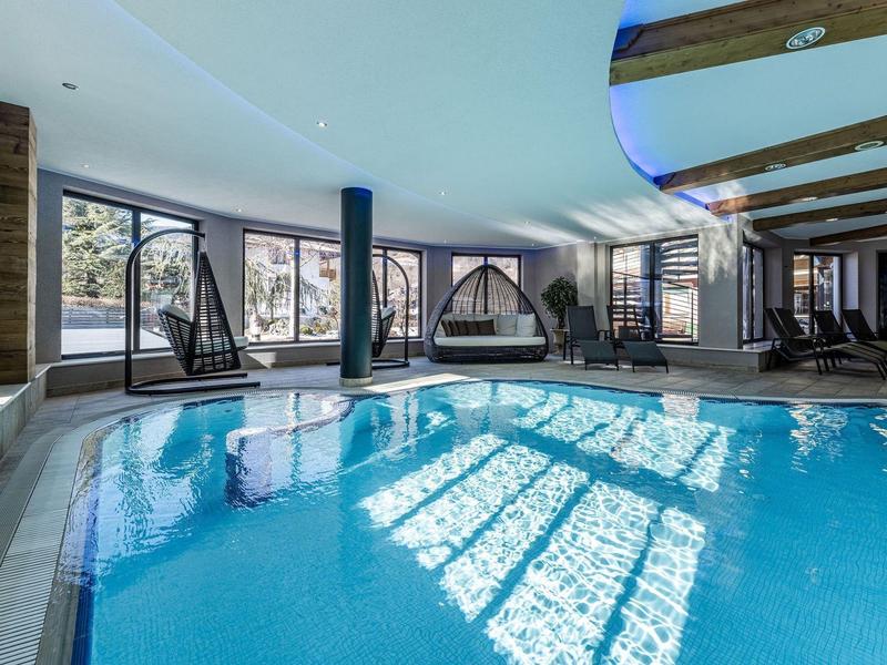Piscina coperta con grandi finestre e sedie sospese in un'atmosfera rilassante da hotel.