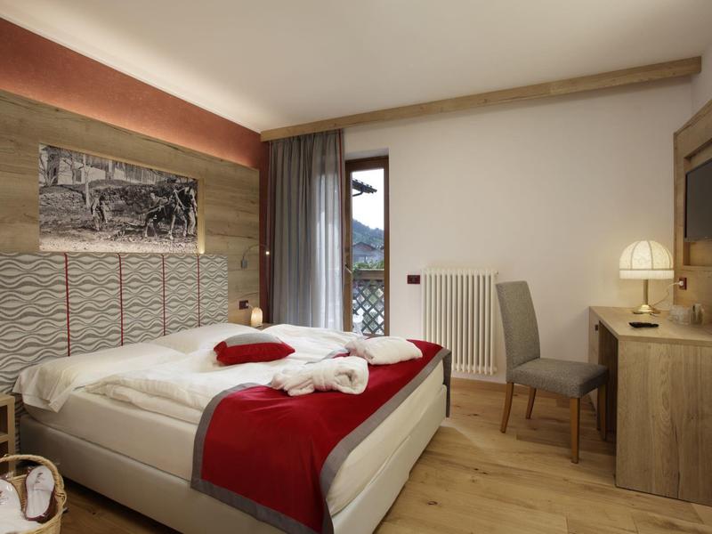 Camera d'albergo moderna con letto matrimoniale, scrivania e balcone con vista sulle montagne.