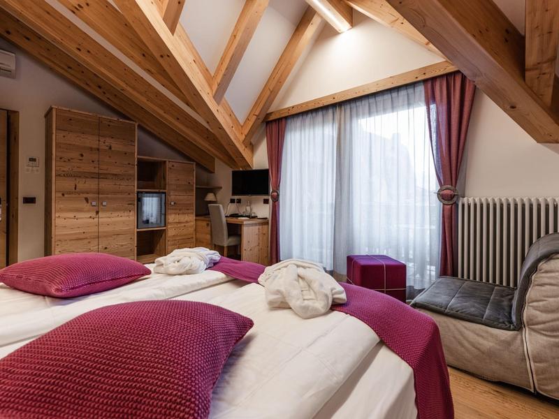 Accogliente camera d'hotel sotto soffitti inclinati con due letti e pannelli in legno.