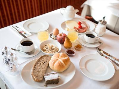 Ontbijttafel met broodjes, brood, koffie, sap en jam geserveerd op een wit tafelkleed.