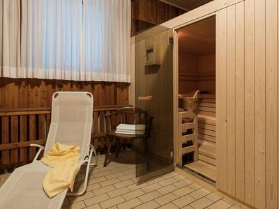 Houten sauna met glazen deur, ontspanningsruimte met ligstoel en handdoek.