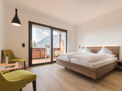 Modern hotelkamer met tweepersoonsbed, balkon en bergzicht bij daglicht.