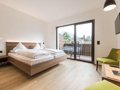 Lichte hotelkamer met tweepersoonsbed, houten vloer, balkon en modern interieur.