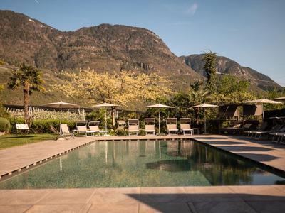 Basen rekreacyjny z leżakami i parasolami na tle górskiego krajobrazu.