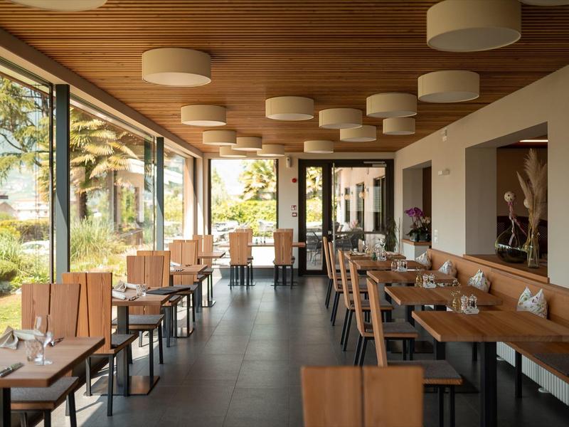 Modern restaurant met houten meubels en groot panoramisch raam met uitzicht op palmbomen.