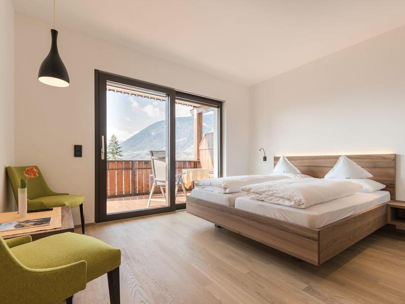 Modern hotelkamer met tweepersoonsbed, balkon en bergzicht bij daglicht.