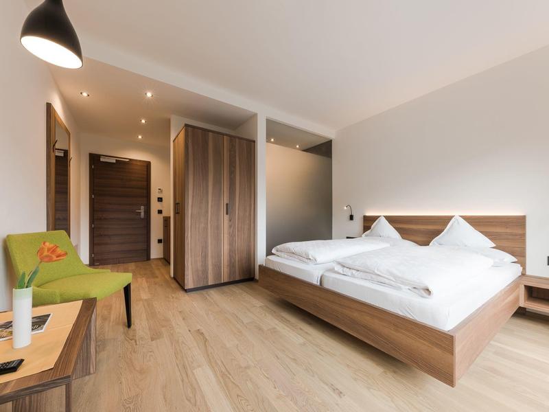 Moderne hotelkamer met tweepersoonsbed, groene stoel en houten vloer
