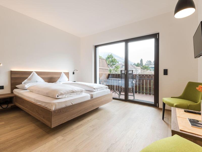Lichte hotelkamer met tweepersoonsbed, houten vloer, balkon en modern interieur.