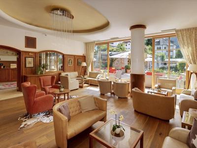 Gemütlicher Hotel-Lounge mit Ledersesseln, Holzboden und großen Fenstern zum Garten.