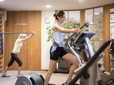 Two women exercise in a modern gym with wooden paneling and equipment.
