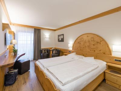 Bright hotel room with double bed, desk, chair, and window with curtains.