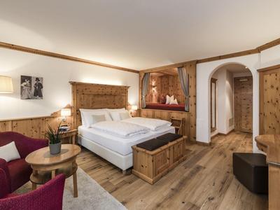 Cozy hotel room with a large bed, wooden decor, and red-purple seating furniture.