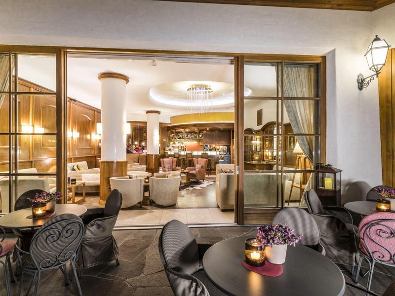 Cozy hotel lounge with open doors leading to a terrace with tables and chairs in evening light.